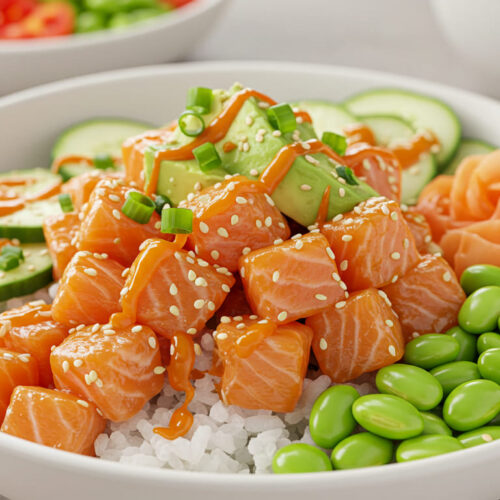 Homemade salmon poke bowl topped with avocado slices, edamame, sesame seeds, and crispy onions on a bed of seasoned rice.