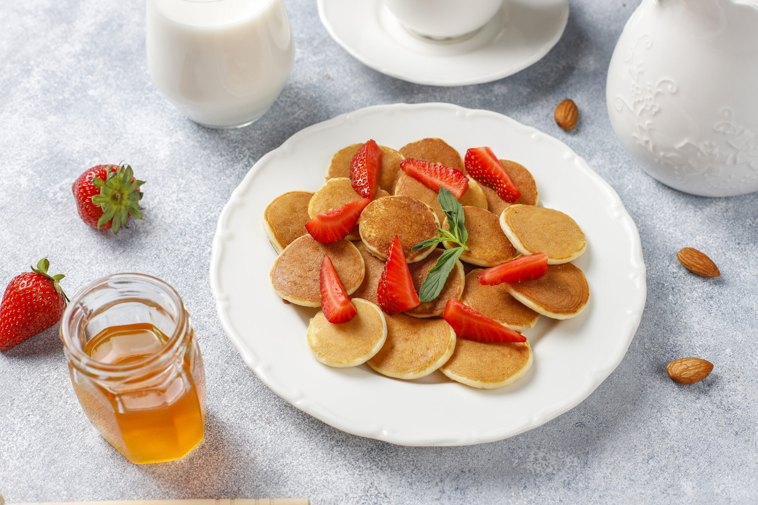 A plate of golden-brown mini pancakes stacked neatly, drizzled with maple syrup and topped with fresh blueberries and strawberries.